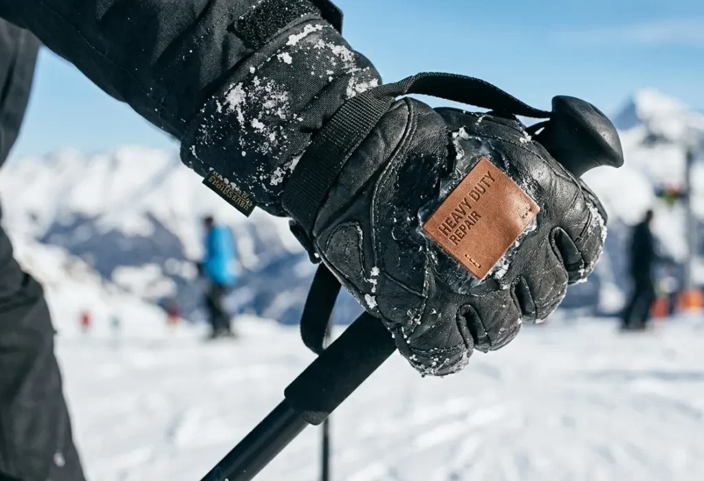 Field testing a patched ski glove tear by gripping a ski pole tightly in the snow to ensure the adhesive holds