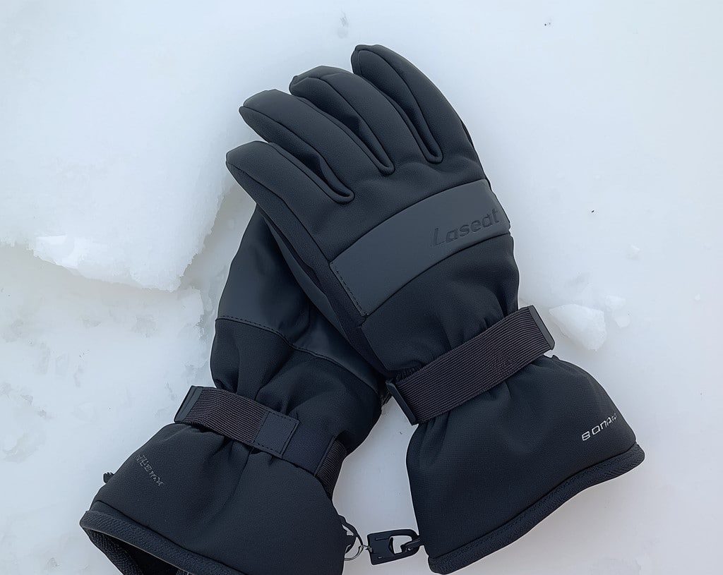 A pair of worn ski gloves resting on snow, illustrating how cold weather affects ski glove insulation and loft over multiple seasons.
