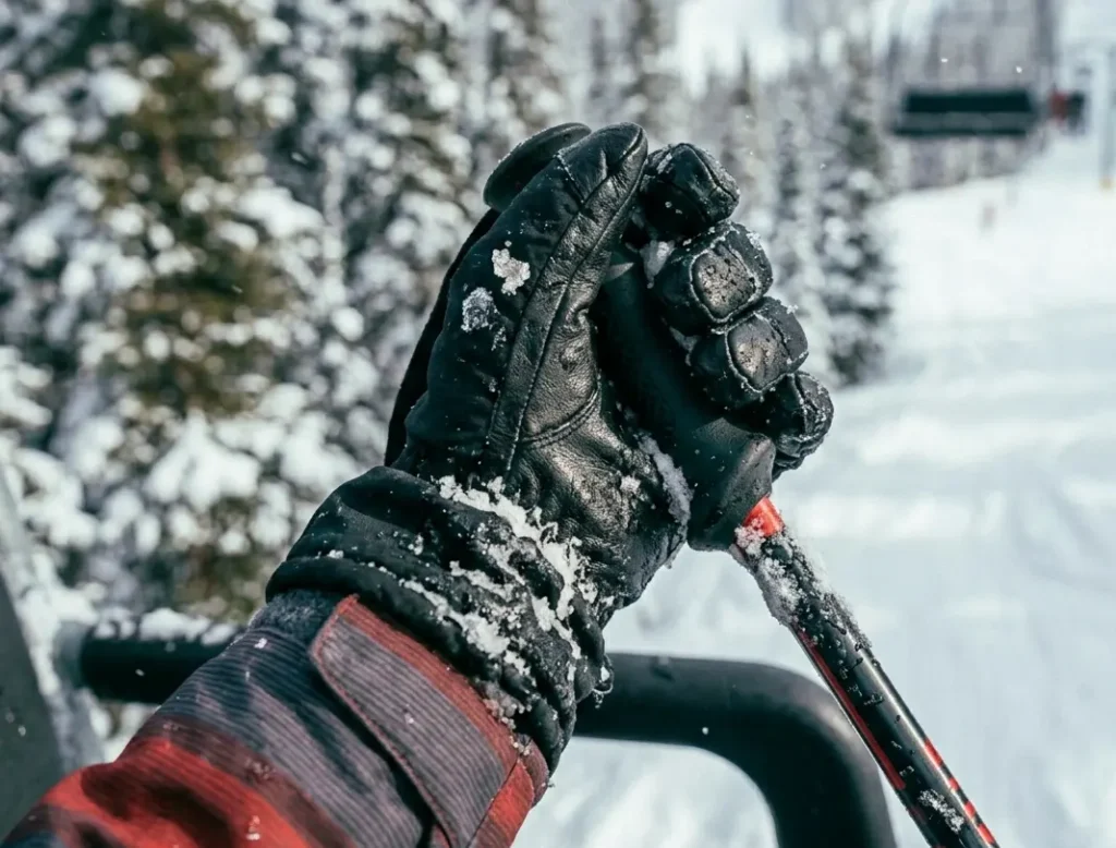 Ski gloves covered in wet snow while gripping a ski pole on a chairlift